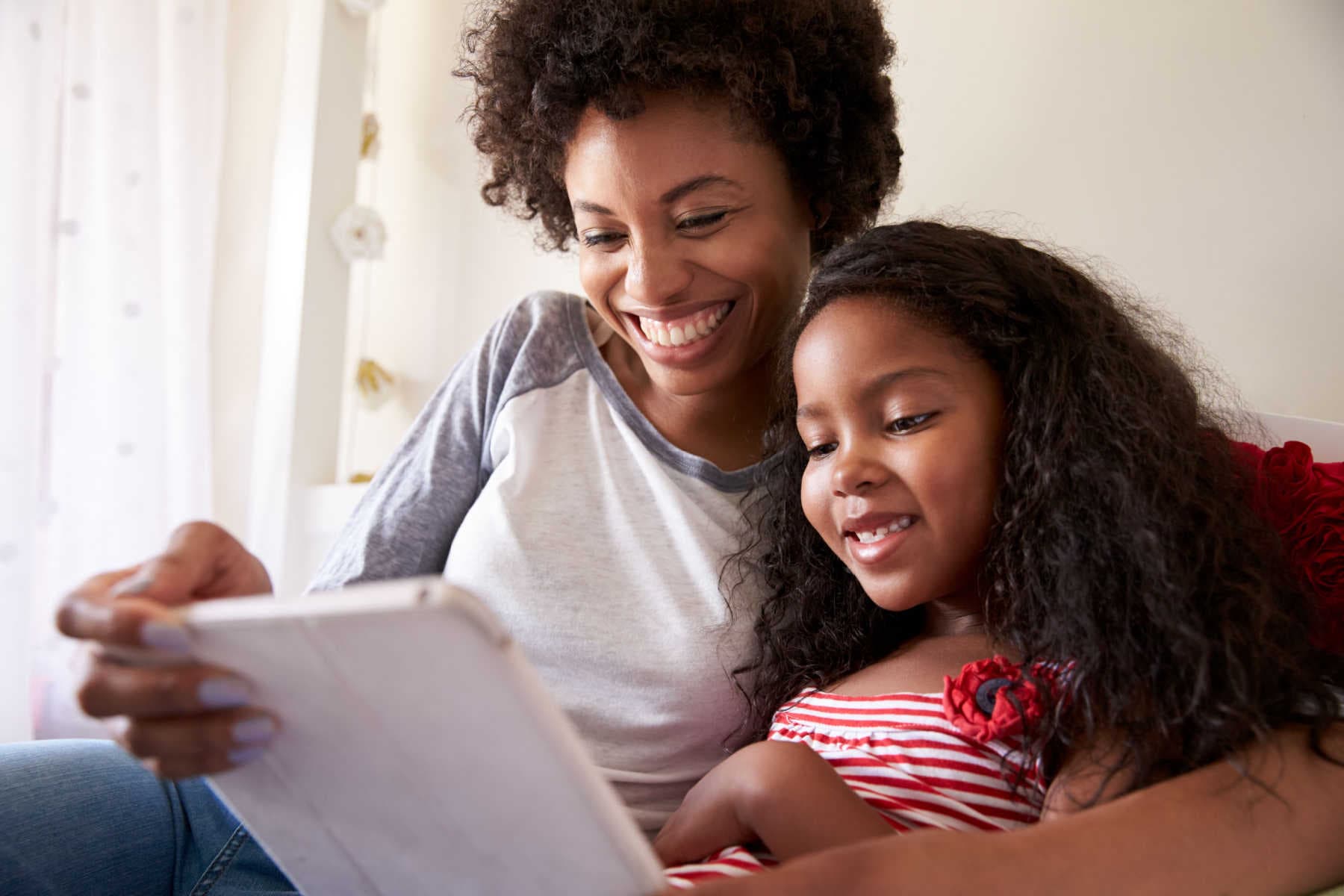 A mom and her daughter looking at a tablet.